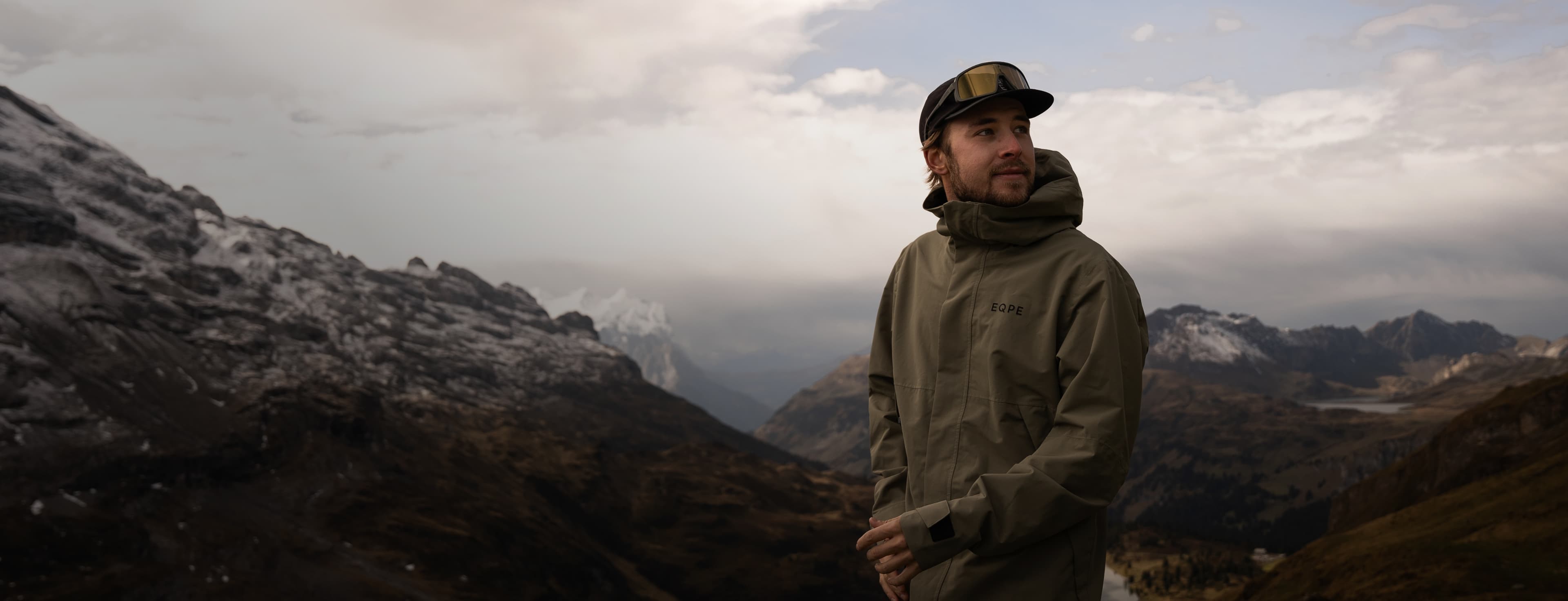 A hiker in a green outdoor jacket stands in a mountainous landscape.